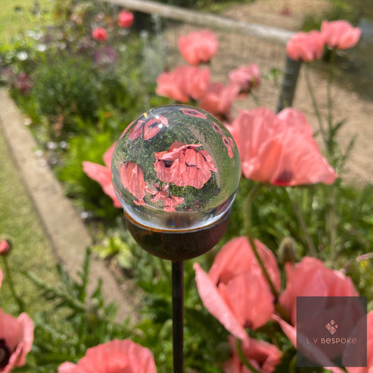 Clear glass orb garden stake reflecting pink poppies in a border