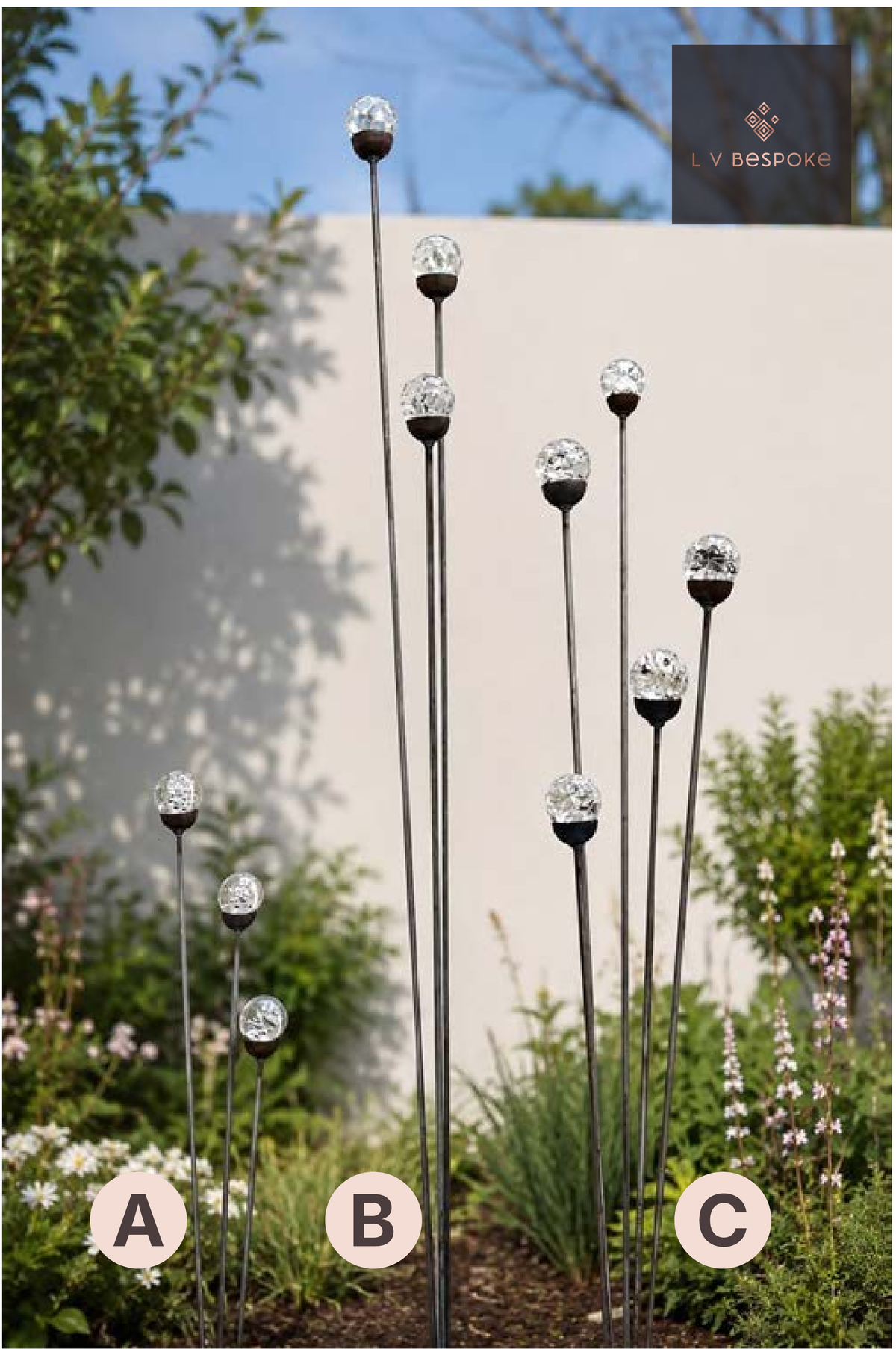 Raw steel glass orb garden stakes at staggered heights, planted in a border