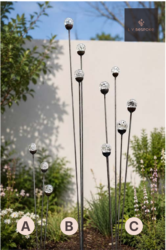 Raw steel glass orb garden stakes at staggered heights, planted in a border