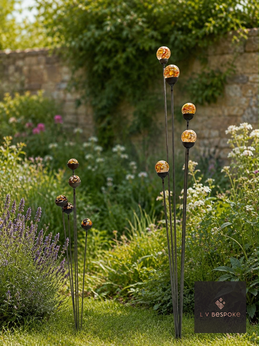 Raw steel short and tall clusters of five garden stakes with amber glass marbles, planted in a border