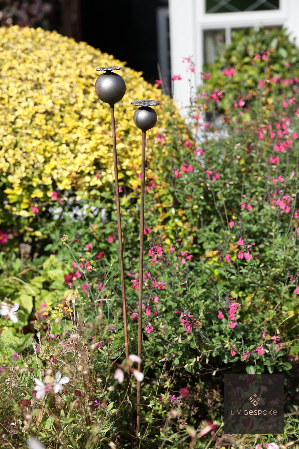 Raw steel Large Poppy Head flower head on a garden stake, planted in a border