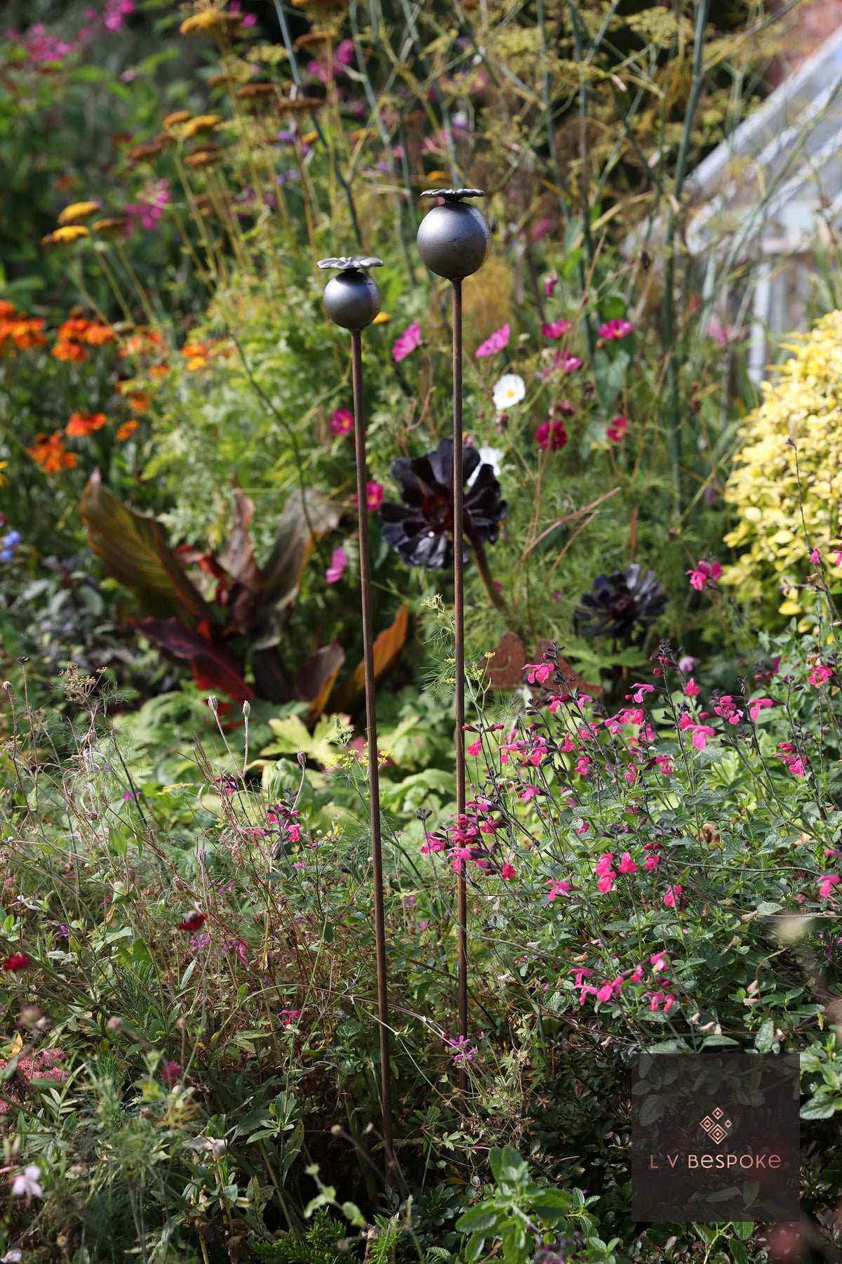 Raw steel Small Poppy Head flower head on a garden stake, planted in a border
