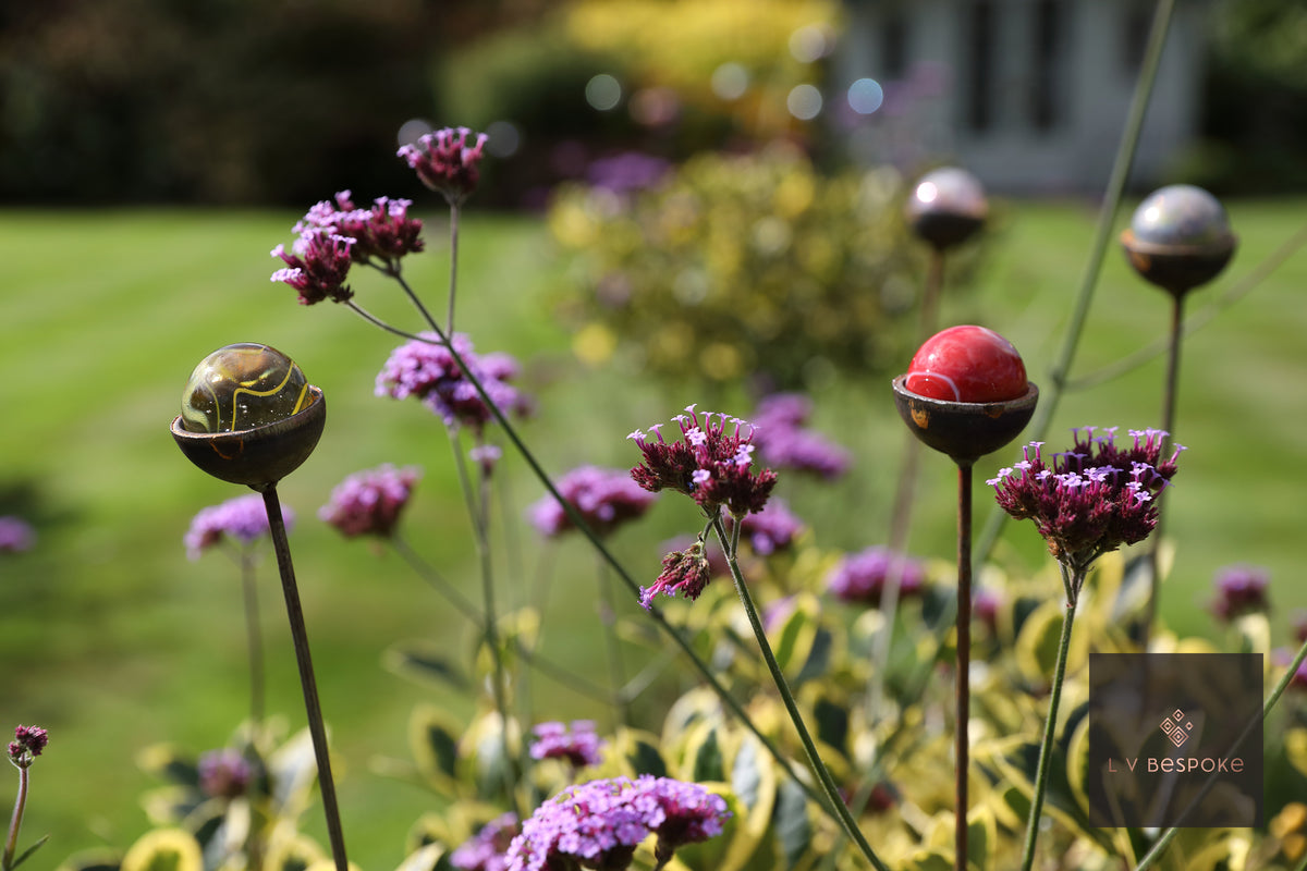 Raw steel sun catcher stakes topped with coloured glass marbles at different heights, planted in a border