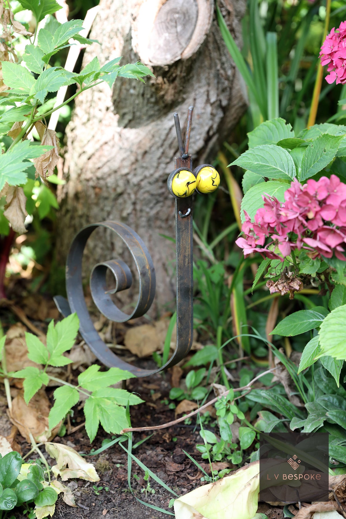 Raw steel snail with a scrolled spiral shell and glass marble eyes, planted in a border