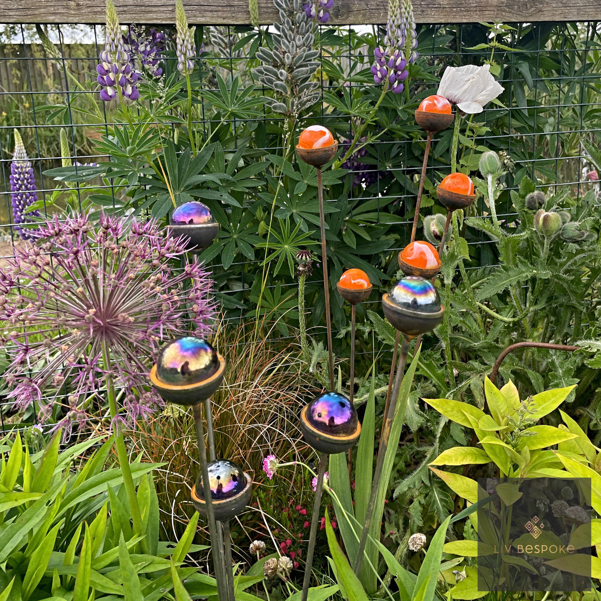 Marble sun catchers at different heights among alliums and lupins in a garden border