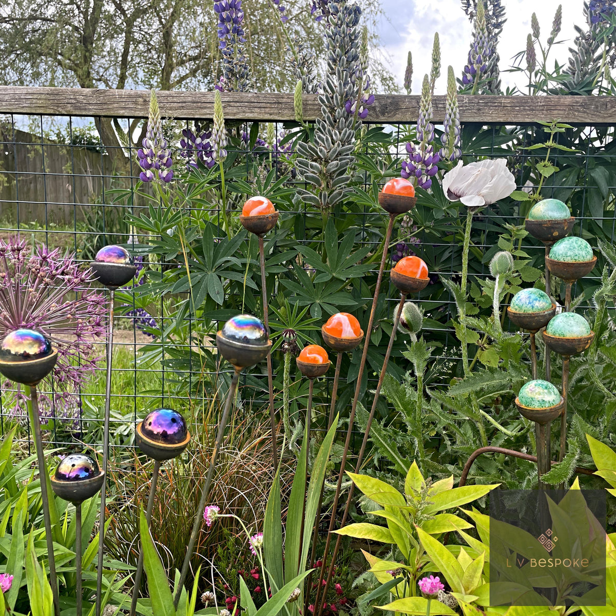Colourful marble sun catcher stakes swaying in a planted garden border