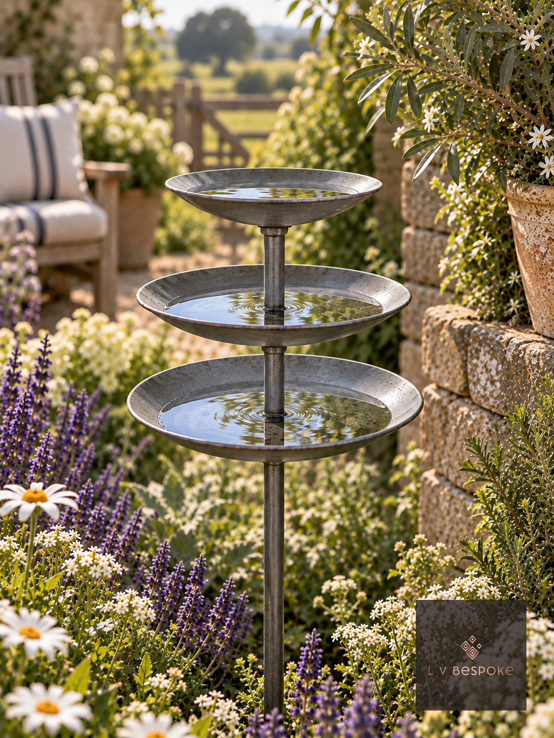 Triple tier steel bee drinker with three round dishes on a stem in a cottage garden border